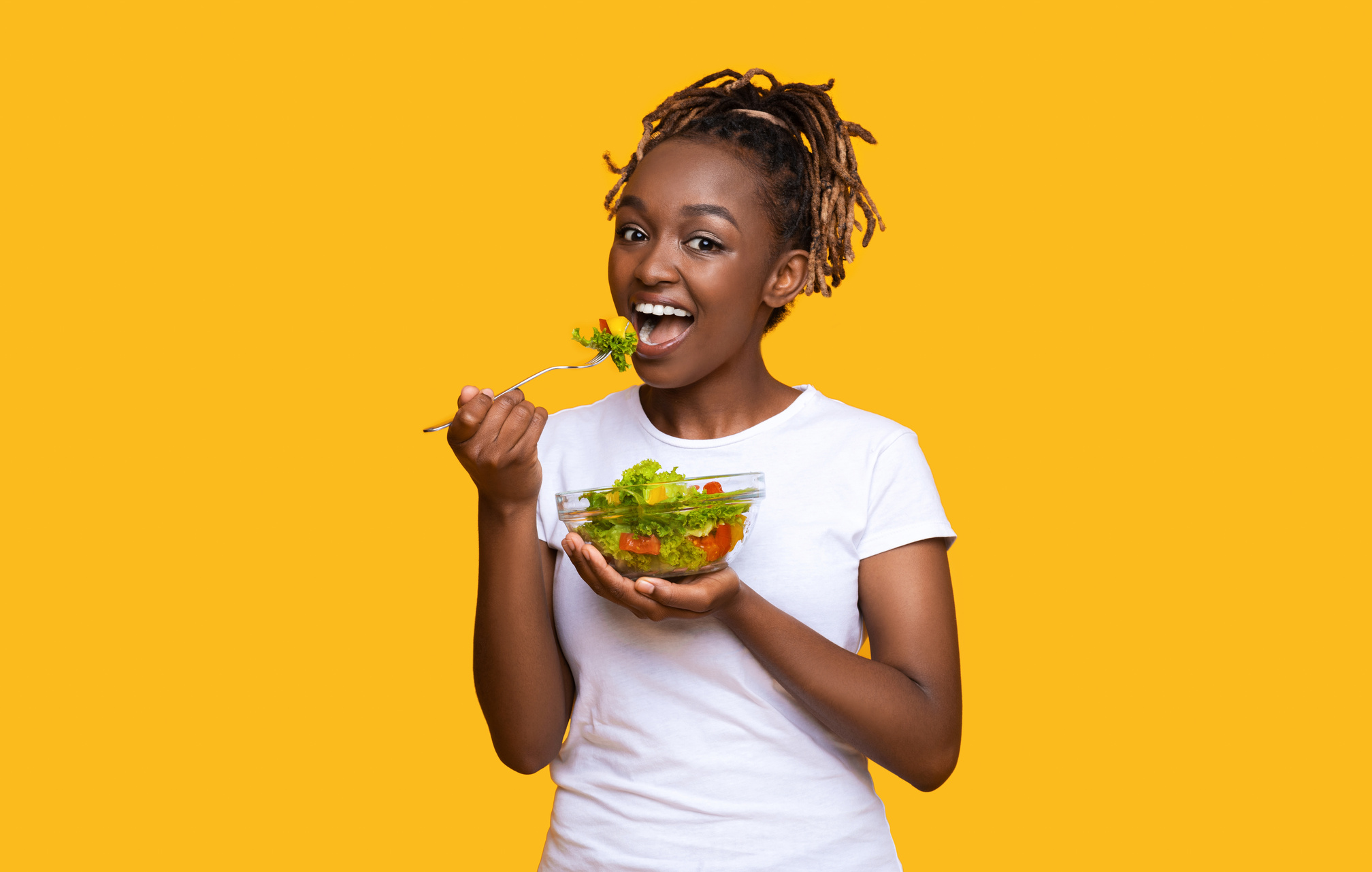 Healthy black lady eating fresh salad over yellow